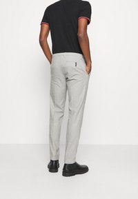 Světlé šedé kalhoty s přiléhavým střihem, vybavené bočními kapsami a hladkou strukturou. Nosené s černou košilí a černými botami.