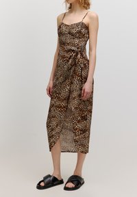 Leopardenmuster Midi-Kleid mit verstellbaren Spaghetti-Trägern, einem taillierten Oberteil und einem gebundenen Taillendetail. Kombiniert mit schwarzen Riemchensandalen.