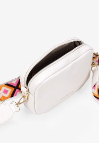 Bolso cruzado de cuero vegano blanco con cierre de cremallera. Presenta una correa de patrón colorido y sutiles acentos en oro.