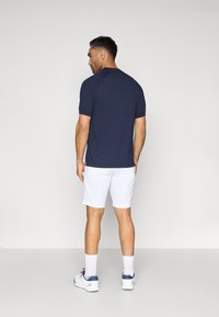 Ναυτικό μπλουζάκι κοντομάνικο με στρογγυλή λαιμόκοψη, συνδυασμένο με λευκές βερμούδες και λευκά αθλητικά παπούτσια, θέα από πίσω.