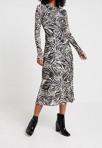 Långärmad midiklänning med ett svart och krämfärgat zebramönster, tillverkad av ett mjukt tyg. Svarta ankelboots fulländar looken.