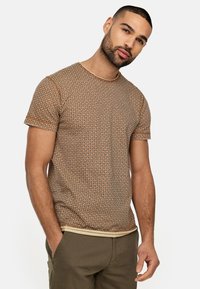 Brun mønstret T-shirt med rund hals og korte ærmer, der har et subtilt geometrisk design og en kontrastfarvet kant ved kanten.