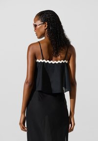 Fekete felső fehér, hullámos szegéllyel, ujjatlan kialakítású, laza szabású, könnyű anyagból készült, áramló szerkezettel.