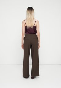 Pantaloni a gamba larga marroni con una texture liscia, dotati di tasche posteriori. Abbinati a un top in satin bordeaux, con spalline sottili.