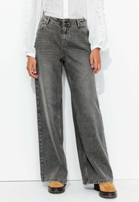 Jean large gris foncé à taille haute, comportant un design classique à cinq poches et un léger délavage. Associé à des bottes chunky beige.