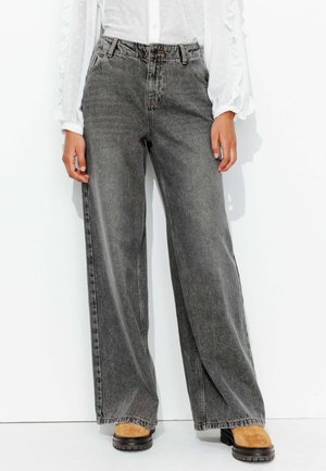 Jean large gris foncé à taille haute, comportant un design classique à cinq poches et un léger délavage. Associé à des bottes chunky beige.