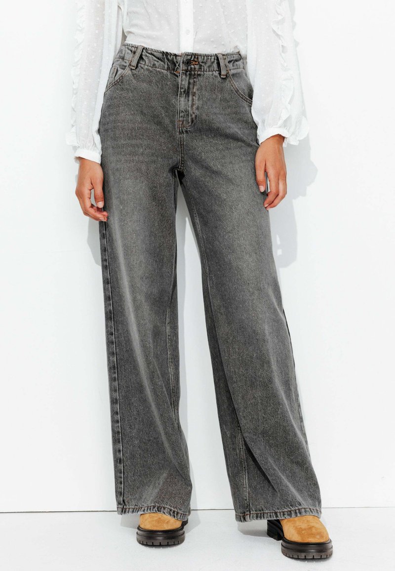 Jean large gris foncé à taille haute, comportant un design classique à cinq poches et un léger délavage. Associé à des bottes chunky beige.