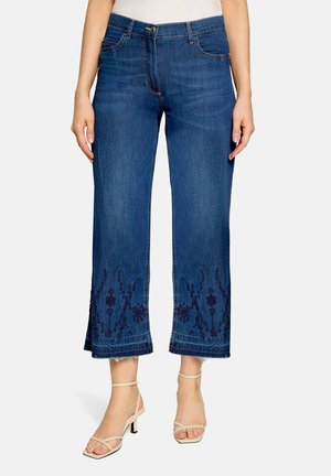Blå korte jeans med blomsterbroderi og frynser i kanten, båret med beige remsandaler med hæl.