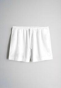 Weiße Freizeitsommerhosen mit elastischem Bund und Kordelzug, flach auf einer schlichten hellgrauen Oberfläche liegend.