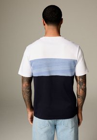 Kortärmad t-shirt med en vit övre del, en ljusblå randig mittendel och en mörkblå nedre del. Mjukt bomullsmaterial.