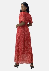 Maxi dress in red with small white floral pattern, short sleeves, cinched waist, and flowing fabric. Paired with black heeled shoes.