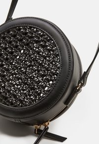 Borsa a tracolla rotonda nera con centro tessuto intrecciato e dettagli in oro sulla cerniera, su sfondo bianco.