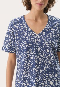 Blå och vit kortärmad t-shirt med V-ringning, med en texturerad tyg och ett abstrakt mönster över hela.