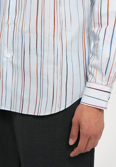 Chemise blanche à manches longues avec des rayures verticales multicolores, possède un ourlet arrondi et des détails de rayures de poignet contrastants. Le tissu semble lisse.