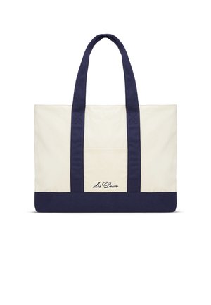 Plátenná taška s krémovým telom, námorníckym modrým dnom a rúčkami. Má vonkajšiu kapsu a vyšívané logo „Les Deux“ v kurzíve.