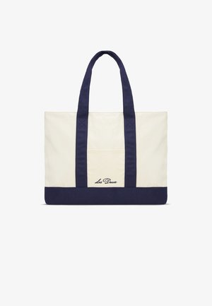 Kangaskassi, jossa vaalea varsi, tummansininen pohja ja kahvat. Varustettu ulkotaskulla ja kirjailulla, jossa cursive-kirjaimilla "Les Deux" -brändäys.