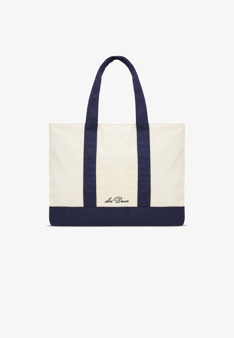Τσάντα τσόχα καμβά με κρεμ σώμα, μπλε σκούρο κάτω μέρος και χερούλια. Διαθέτει εξωτερική τσέπη και κεντημένο λογότυπο "Les Deux" σε γραφή με καλλιγραφικά γράμματα.