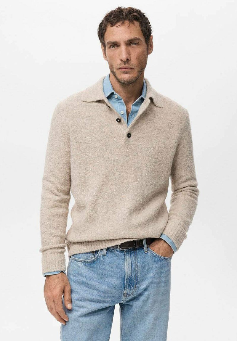 Beżowy sweter z kołnierzykiem, trzema guzikami i teksturowaną tkaniną, noszony na jasnoniebieskiej koszuli i zestawiony z jasnoniebieskimi dżinsami.
