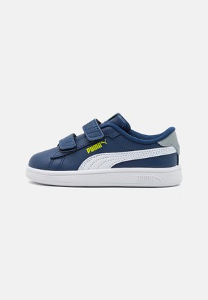 Baskets Puma bleu marine avec semelle blanche, bande blanche, logo Puma jaune fluo et deux brides auto-agrippantes, présentées sur un fond blanc.