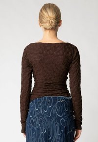 Brun tekstureret langærmet top med en rynket design, parret med blå denim med et bølget mønster og frynset talje.