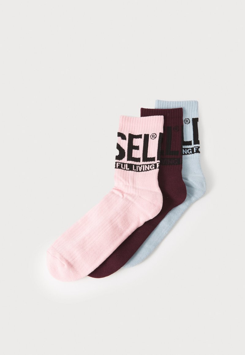 Tre paia di calzini nei colori rosa, bordeaux e azzurro chiaro. Ogni calzino presenta una texture a coste e un logo nero "DIESEL" in cima.