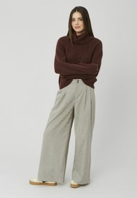 Pull à col roulé bordeaux avec poignets côtelés associé à un pantalon large à carreaux avec un pli avant et un accent bouton.