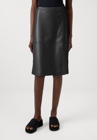 Zwarte leren kokerrok met een gladde textuur, middenlange ontwerp en minimale stikdetails, gecombineerd met zwarte instap sandalen.