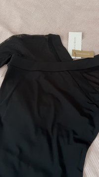 Črn bodi z dolgimi rokavi in gladko teksturo. Ima prosojen zgornji del in oznako, ki označuje reciklirane materiale.