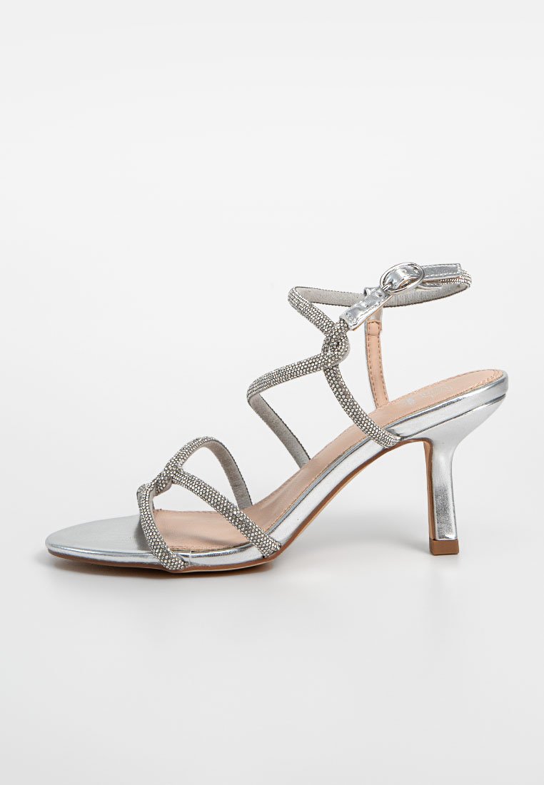 Zilveren hoge hak sandaal met meerdere banden versierd met kleine heldere stenen. Kenmerkt zich door een slank ontwerp en een fijne hak.
