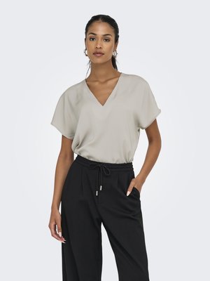 Blouse beige clair à col en V et manches courtes. Associée à un pantalon noir taille haute avec cordon de serrage et détails de plis.