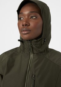 Veste vert olive avec un col haut et une capuche ajustable. Présente une fermeture à zip et un tissu texturé. Design minimal avec des accents pratiques.