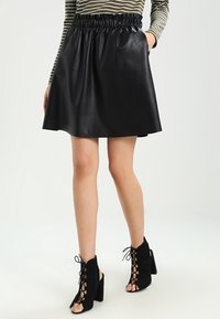 Černá sukně z umělé kůže s elastickým pasem, rozšířeným střihem a bočními kapsami, doplněná o černé laced ankle boots s otevřenou špičkou.