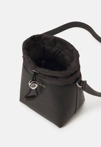 Czarna torba z sztucznej skóry z miękkim, ściąganym wierzchem. Zawiera okrąły akcent z srebrnego metalu oraz regulowany pasek. Teksturowana powierzchnia.