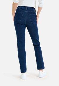 Jean en denim bleu foncé avec une coupe droite, deux poches arrière et un ourlet propre, associé à des baskets blanches.