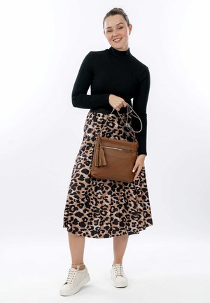 Sac à main en cuir marron avec des franges, porté par une personne en pull noir et jupe à imprimé léopard. Des baskets blanches complètent le look.