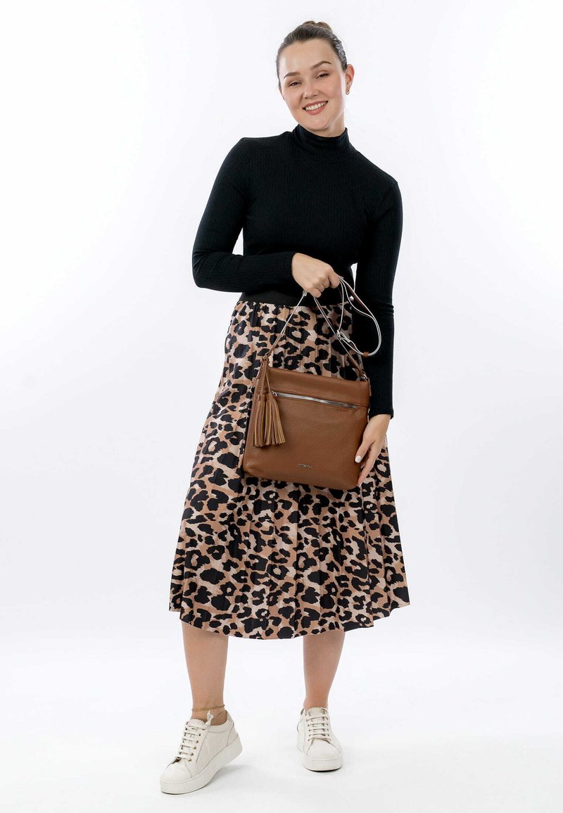 Bolso de cuero marrón con flecos, llevado por una persona con un suéter negro y una falda de estampado de leopardo. Zapatillas blancas completan el conjunto.