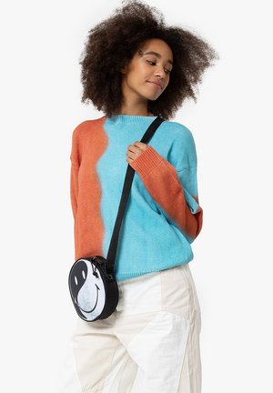 Maglione a blocchi di colore arancione e turchese, con maniche lunghe. Borsa a tracolla nera con un design di faccina sorridente bianca e chiusura con zip.