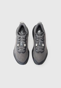 Baskets de sport grises avec une tige en maille, des accents réfléchissants et des motifs texturés. Présentent des lacets gris et une semelle en caoutchouc noire.