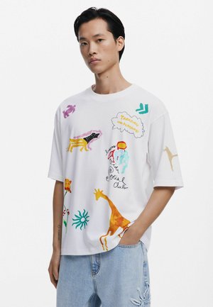 T-shirt bianca a maniche corte con motivi colorati di animali e astratti, con una vestibilità rilassata e scollo rotondo.