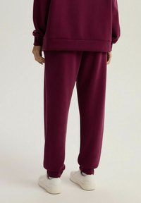 Burgundowa bluza i dopasowane dresy wykonane z miękkiego materiału, z mankietami u kostek i luźnym krojem. Białe sneakersy dopełniają strój.