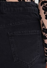 Jean en denim noir avec une poche arrière, des coutures visibles et une texture lisse. Les points forts du design incluent une taille haute.