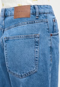 Ανοιχτό μπλε τζιν με πίσω τσέπη και καφέ ετικέτα της μάρκας Topshop, φορεμένο με λευκό μπλουζάκι με ανθισμένο μοτίβο.