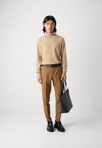 Bež turtleneck pulover, rjave elegantne hlače, črn pas in črna torba za čez ramo. Črne čevlje z debelim podplatom. Enostaven dizajn, nevtralne barve.