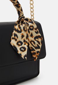 Czarna torebka syntetyczna z złotym łańcuchem, z dodatkiem w postaci chustki w panterkę przewiązanej przy uchwycie.