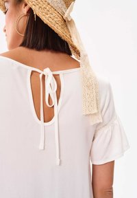 Witte blouse met korte mouwen, voorzien van een striksluiting aan de achterkant en kantdetails langs de mouwen. Zachte stof, ontspannen pasvorm.