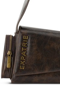 Sac en simili cuir marron avec une texture lisse, présentant une fermeture éclair dorée et le nom de la marque « EXPATRIE » embossé en lettres dorées.