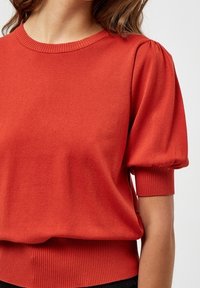 Punainen neulottu paita, jossa on lyhyet röyhelöhihat, resorit kaula-aukossa ja helmassa, sileäpintainen ja rento istuvuus.