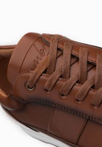 Bruine leren sneaker met een gestructureerd oppervlak, ronde neus en stoffen veters. Voorzien van een logodetail op de tong en een rubberen zool.
