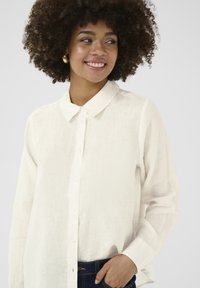 Lightweight, cream-colored linen shirt with a button-up front and a classic collar. Features long sleeves and a relaxed fit.