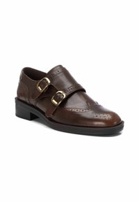 Zapato de cuero marrón con doble hebilla, detalles de brogue y un tacón bajo. Acabado suave con una puntera ligeramente puntiaguda.